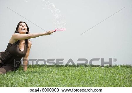 Stock Image - Woman sitting on the ground looking up at bubbles. Fotosearch