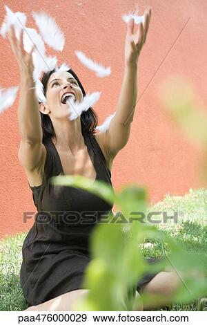 Woman sitting on the ground with arms raised to catch feathers, smiling View Large Photo Image Stock Photo - Woman sitting on the ground with arms raised to catch feathers, smiling. Fotosearch