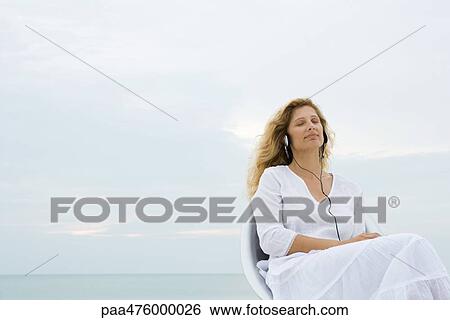 Woman sitting outdoors listening to headphones with eyes closed View Large Photo Image Stock Photograph - Woman sitting outdoors listening to headphones with eyes closed. Fotosearch