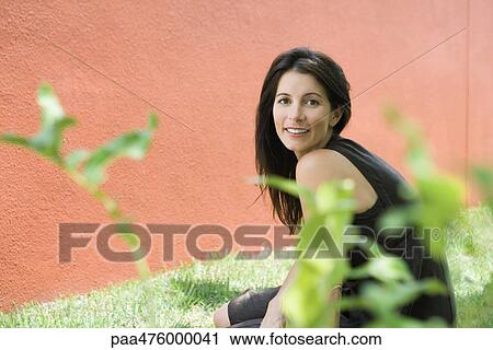Woman sitting outdoors looking over shoulder at camera, portrait View Large Photo Image Stock Image - Woman sitting outdoors looking over shoulder at camera, portrait. Fotosearch