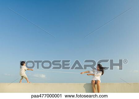 Stock Image - Boy and woman playing tug of war, blue sky in background. Fotosearch