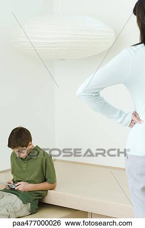 Boy playing video game, mother watching, hands on hips View Large Photo Image Stock Photograph - Boy playing video game, mother watching, hands on hips. Fotosearch