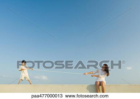 Stock Image - Little boy and woman playing tug of war, blue sky in background. Fotosearch