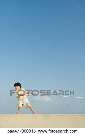Stock Photography - Little boy pulling on rope, blue sky in background, full length. Fotosearch