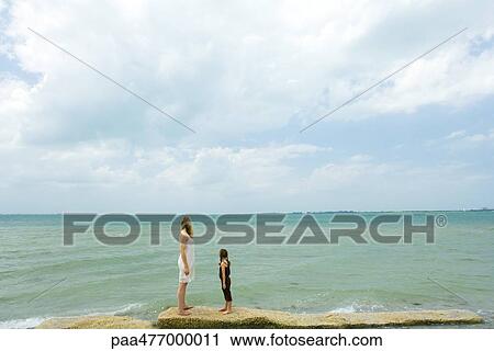 Mother and daughter standing by ocean, looking toward horizon, full length View Large Photo Image Stock Image - Mother and daughter standing by ocean, looking toward horizon, full length. Fotosearch