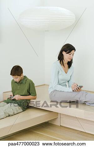 Woman and son sitting near each other, woman using PDA, boy playing with handheld video game View Large Photo Image Stock Image - Woman and son sitting near each other, woman using PDA, boy playing with handheld video game. Fotosearch