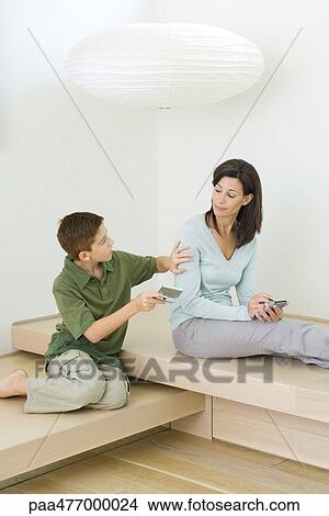 Woman and son sitting together, boy showing mother handheld video game View Large Photo Image Picture - Woman and son sitting together, boy showing mother handheld video game. Fotosearch
