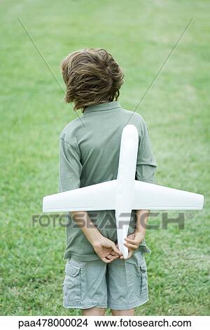 Picture - Boy holding toy airplane behind back, rear view. Fotosearch