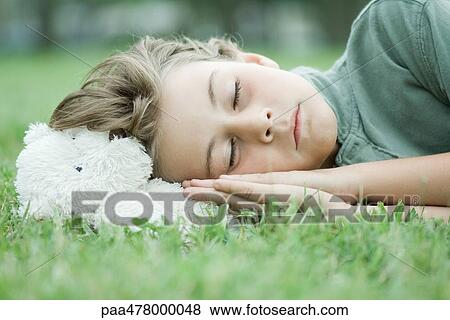 Stock Photo - Boy resting head on teddy bear, sleeping on grass. Fotosearch