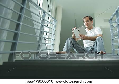 Man sitting on stairs, reading book, low angle view View Large Photo Image Stock Photograph - Man sitting on stairs, reading book, low angle view. Fotosearch