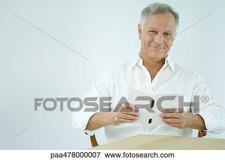 Stock Photo - Mature man reading book, smiling at camera. Fotosearch