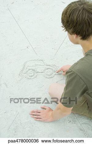 Stock Photograph - Teen boy drawing car in sand. Fotosearch