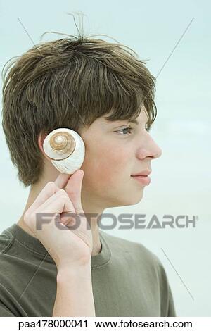 Teen boy holding up seashell to ear, profile View Large Photo Image Stock Image - Teen boy holding up seashell to ear, profile. Fotosearch