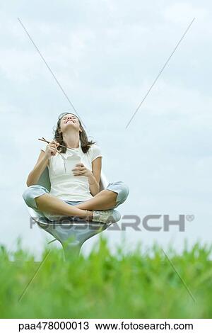 Stock Image - Teen girl sitting eating Chinese takeout, head back, low angle view. Fotosearch