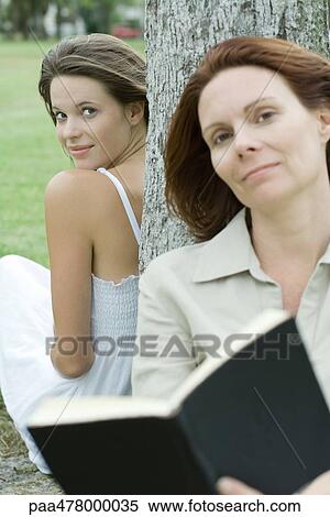 Woman and teen girl leaning against tree trunk, woman holding book View Large Photo Image Stock Photography - Woman and teen girl leaning against tree trunk, woman holding book. Fotosearch