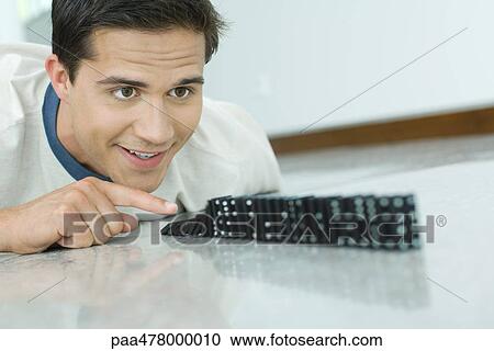 Young man knocking over line of dominos View Large Photo Image Stock Image - Young man knocking over line of dominos. Fotosearch