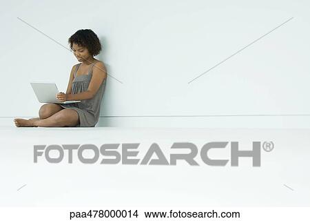 Picture - Young woman sitting on floor, using laptop. Fotosearch