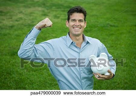 Man holding piggy bank, raising fist and smiling at camera View Large Photo Image Stock Photo - Man holding piggy bank, raising fist and smiling at camera. Fotosearch