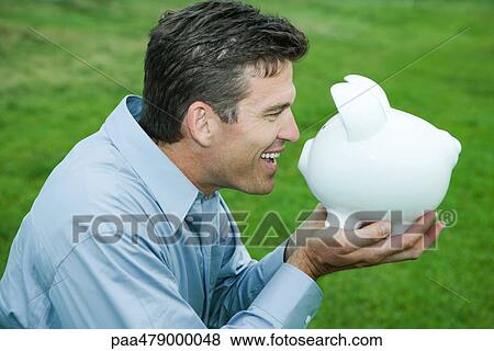 Man holding up piggy bank to face, smiling, side view View Large Photo Image Stock Photo - Man holding up piggy bank to face, smiling, side view. Fotosearch