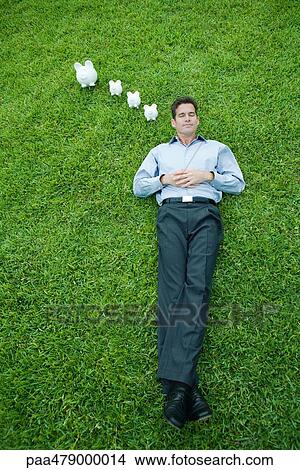 Man lying on grass with eyes closed, piggy banks next to head View Large Photo Image Picture - Man lying on grass with eyes closed, piggy banks next to head. Fotosearch