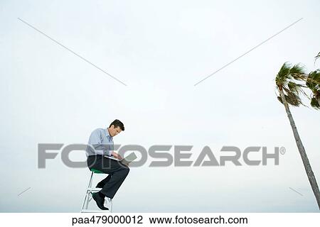 Man sitting in wind, using laptop, low angle view View Large Photo Image Stock Image - Man sitting in wind, using laptop, low angle view. Fotosearch