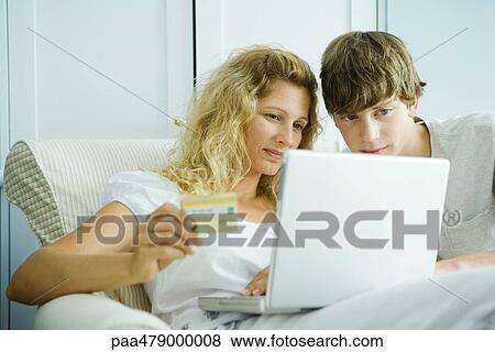 Stock Photo - Woman and teenage son making credit card purchase online. Fotosearch