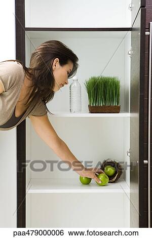 Woman reaching for apple in pantry containing apples in nest, tray of wheat grass and bottle of water View Large Photo Image Stock Photograph - Woman reaching for apple in pantry containing apples in nest, tray of wheat grass and bottle of water. Fotosearch