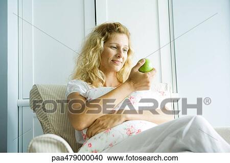 Woman sitting in arm chair, examining apple, smiling View Large Photo Image Stock Image - Woman sitting in arm chair, examining apple, smiling. Fotosearch