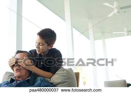 Stock Photo - Boy placing his hands over grandfather's eyes. Fotosearch