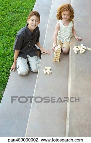 Stock Image - Brother and sister on stairs, playing with blocks together, high angle view. Fotosearch