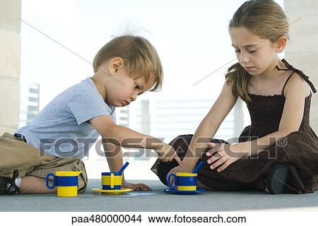 Picture - Brother and sister sitting on the ground, playing with plastic cups. Fotosearch