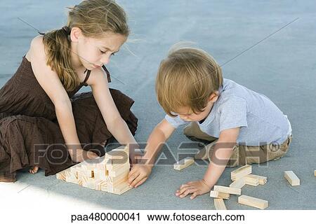 Stock Image - Brother and sister sitting on the ground, playing with building blocks together. Fotosearch
