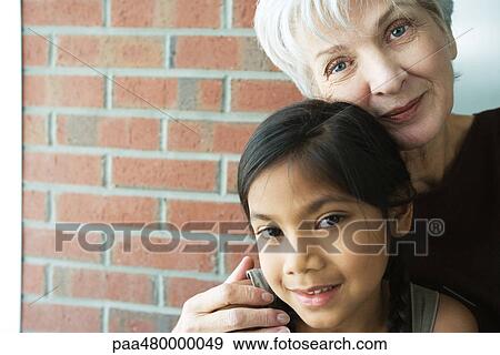 Grandmother embracing granddaughter, both smiling at camera, portrait View Large Photo Image Stock Photo - Grandmother embracing granddaughter, both smiling at camera, portrait. Fotosearch