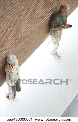 Man and woman leaning against brick wall using cell phones, high angle view View Large Photo Image Stock Image - Man and woman leaning against brick wall using cell phones, high angle view. Fotosearch