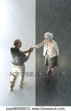 Stock Image - Man shaking woman's hand, high angle view. Fotosearch