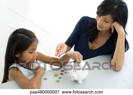 Mother and daughter putting coins in piggy bank together, high angle view View Large Photo Image Stock Photo - Mother and daughter putting coins in piggy bank together, high angle view. Fotosearch