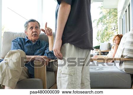 Stock Photo - Senior man sitting in chair, looking up at grandson, cropped view. Fotosearch