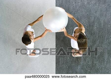 Stock Photography - Teen twin sisters holding up ball together, viewed from directly above. Fotosearch