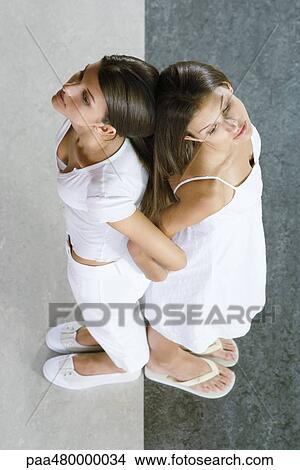 Picture - Twin sisters standing back to back, arm in arm, viewed from directly above. Fotosearch