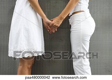 Stock Image - Two teenage girls standing face to face, holding hands, cropped view. Fotosearch