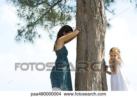 Two young friends playing hide-and-seek, one placing finger on lips and looking at camera View Large Photo Image Picture - Two young friends playing hide-and-seek, one placing finger on lips and looking at camera. Fotosearch