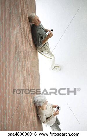 Woman and man standing apart, leaning against wall, holding coffee cups, high angle view View Large Photo Image Stock Photograph - Woman and man standing apart, leaning against wall, holding coffee cups, high angle view. Fotosearch