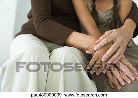 Stock Photo - Woman embracing girl, holding hands, cropped view. Fotosearch