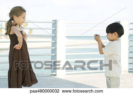 Stock Image - Young boy photographing friend with camera, side view. Fotosearch