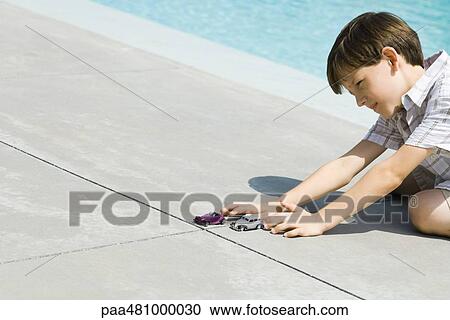 Boy sitting on the ground next to swimming pool, playing with cars, cropped view View Large Photo Image Stock Image - Boy sitting on the ground next to swimming pool, playing with cars, cropped view. Fotosearch