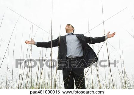 Man in suit standing in tall grass with arms out, looking up, low angle view View Large Photo Image Stock Photography - Man in suit standing in tall grass with arms out, looking up, low angle view. Fotosearch