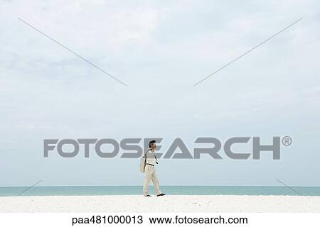 Stock Image - Man in suit walking along beach, side view. Fotosearch