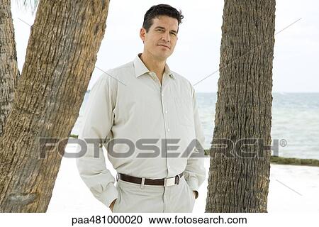 Man standing between tree trunks, hands in pockets, looking at camera View Large Photo Image Stock Image - Man standing between tree trunks, hands in pockets, looking at camera. Fotosearch