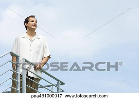Man standing on balcony, looking away, smiling View Large Photo Image Stock Photo - Man standing on balcony, looking away, smiling. Fotosearch