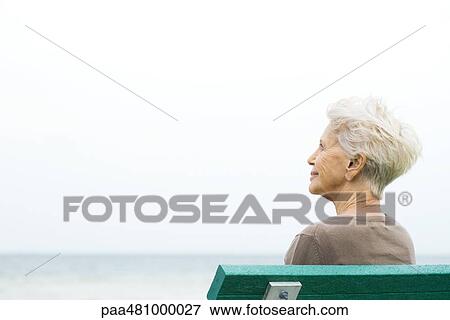 Stock Photo - Senior woman sitting on bench, looking up, rear view. Fotosearch